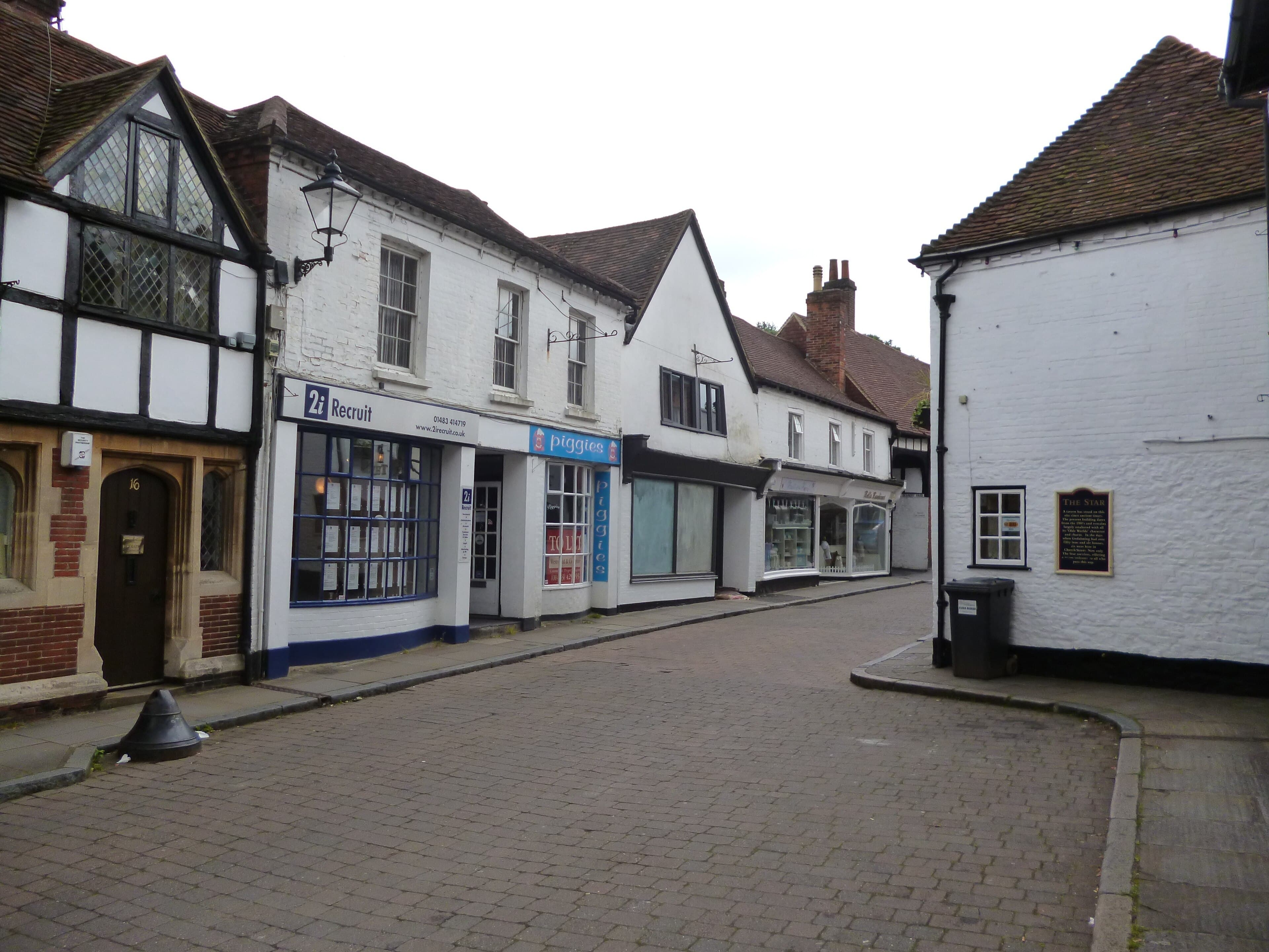 Quiet cobbled street in Godalming lined with whitewashed timber-framed shops and a pub wall on the right