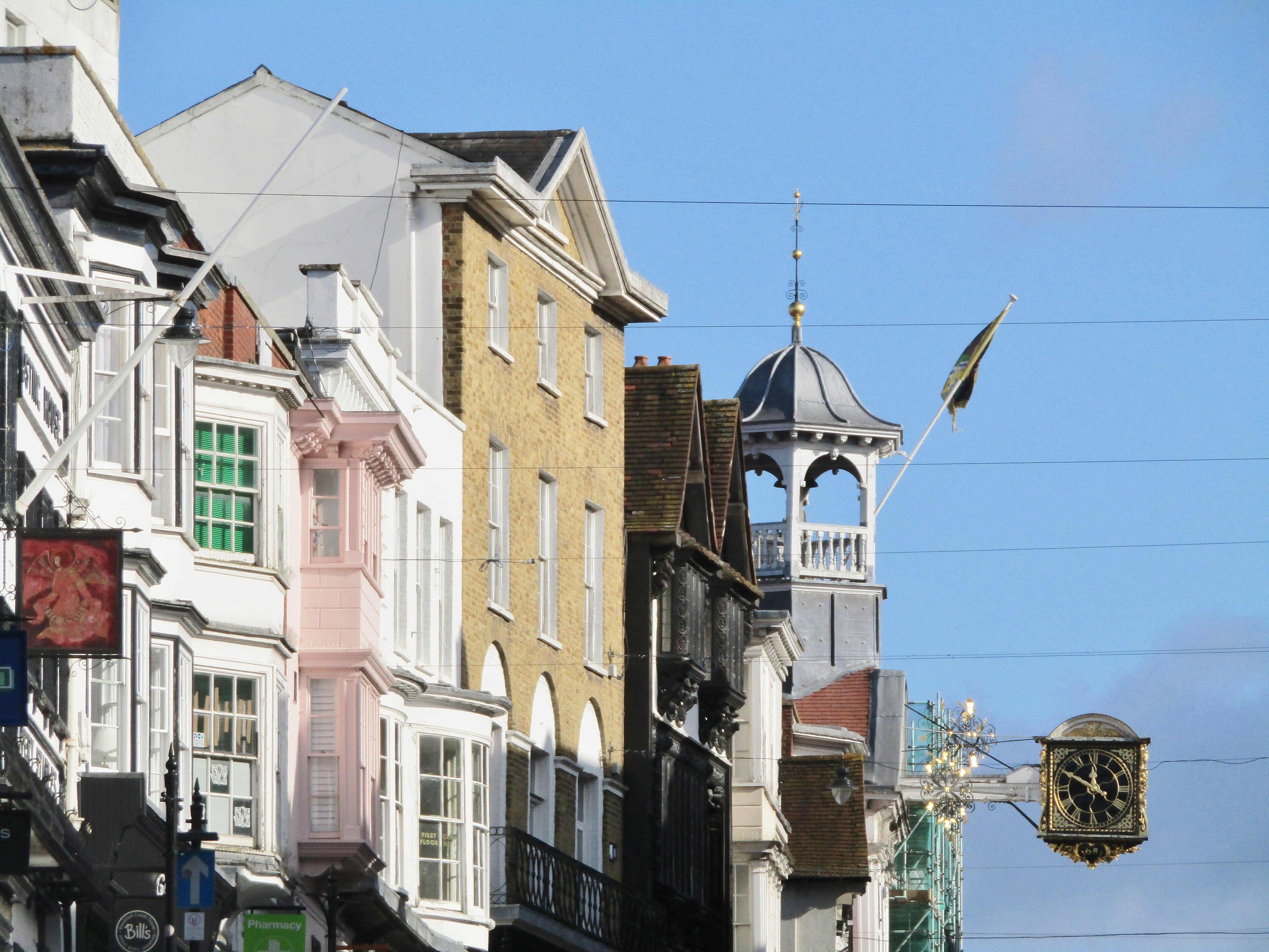 Historic buildings along Guildford High Street with bay windows, a bell turret and the ornate gold projecting clock